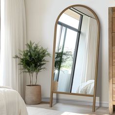 a mirror sitting on top of a wooden dresser next to a plant in a vase