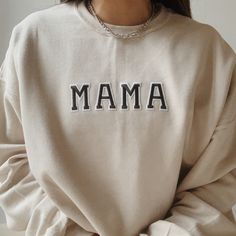 a woman wearing a sweatshirt with the word mama printed on it, sitting in front of a white wall