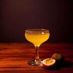 a glass filled with liquid sitting on top of a wooden table next to a piece of fruit