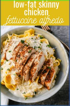 a white bowl filled with chicken and pasta on top of a wooden table next to a fork