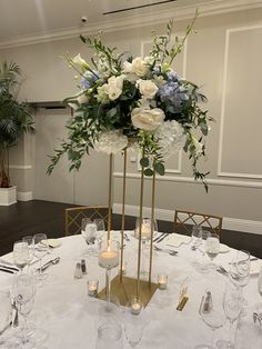 a tall centerpiece with white and blue flowers sits on a round dining room table