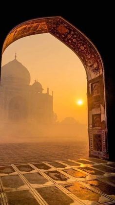 the sun is setting in front of an arch with a view of a building through it