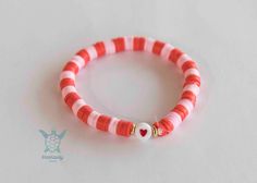 red and white striped bracelet with gold heart charm on the end, sitting on a white surface