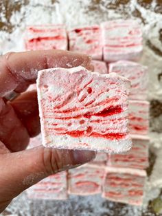 a hand holding up a piece of red and white cake with powdered sugar on top