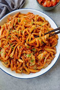 a white bowl filled with noodles and meat on top of a table next to some chopsticks