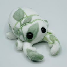 a green and white stuffed animal laying on top of a gray surface with black eyes