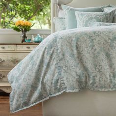 a bed with blue and white comforters in a bedroom next to a dresser filled with flowers