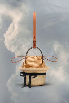 a straw bag with a leather strap hanging from it's side, in front of a cloudy sky