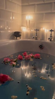 rose petals floating on the surface of a bathtub with candles in the back ground