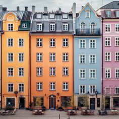 several multicolored buildings with tables and benches in front of them on a cloudy day