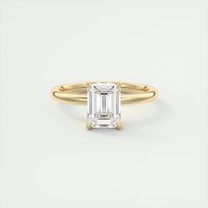 a yellow gold ring with an emerald cut diamond in the center, on a white background