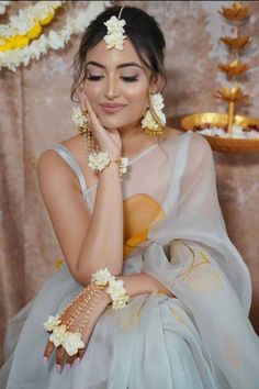 a woman with flowers in her hair sitting on a chair wearing a white and yellow dress