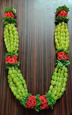 grapes and roses arranged in the shape of a heart on a wooden table with green leaves