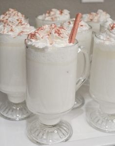 three glasses filled with whipped cream and topped with candy canes on a white table