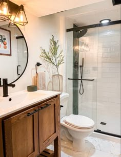 a white toilet sitting next to a walk in shower under a bathroom mirror with lights on it