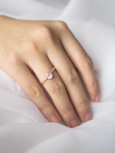 a woman's hand with a diamond ring on top of her finger and white sheets in the background