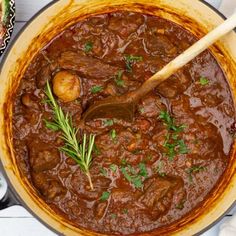 a pot full of stew with a wooden spoon in it and some vegetables on the side