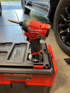 a red and black tool is on top of a box in front of a car