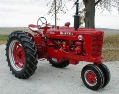 an old red farmall tractor parked on the side of a road in front of a tree