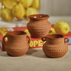 two brown vases sitting on top of a table next to a box of lemons