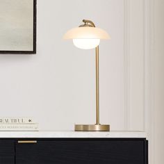 a table lamp sitting on top of a white counter next to a black cabinet and painting