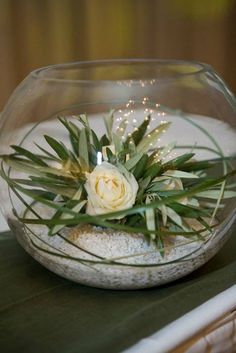 an arrangement of flowers in a glass bowl on a table with sand and seaweed