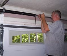 a man is working on an overhead garage door with the help of a window sealer