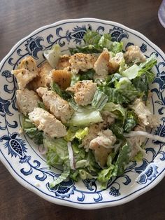 a salad with chicken and lettuce in a blue and white bowl on a wooden table