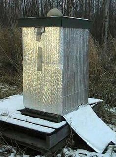 a metal box sitting on top of a snow covered ground in front of some trees