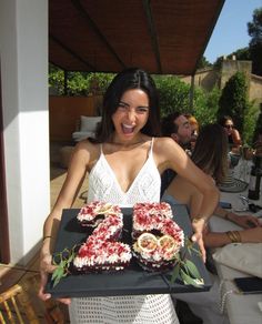 a woman is holding a tray with two cakes on it and smiling at the camera