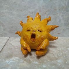 a ceramic yellow sun with its mouth open and eyes wide open, sitting on a stone surface