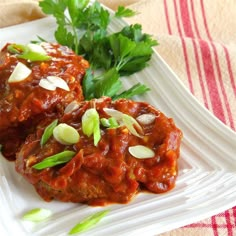 two meatballs covered in sauce and garnished with green onions on a white plate