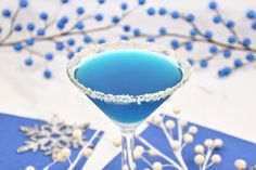 a blue drink in a martini glass with snow flakes on the rim and branches