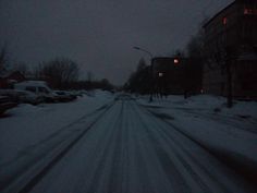 a snowy street with cars parked on the side and buildings in the background at night