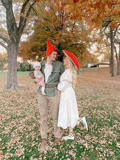 a man and woman are standing in the grass with red hats on their heads while holding a baby