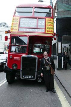 a man standing next to a red double decker bus on the side of the road