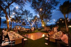 people are sitting at tables with lights strung from the trees in the background and on the ground