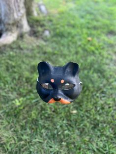 a black cat mask hanging from a tree in the grass with an orange ball attached to it's mouth