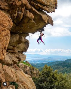 a man climbing up the side of a cliff with his feet in the air while holding onto a rope