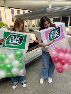 two girls are holding up some big taco boxes with balloons in them and one girl is holding a book