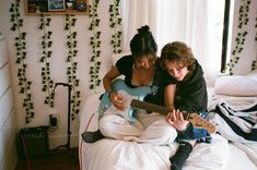 two people sitting on a bed playing guitar