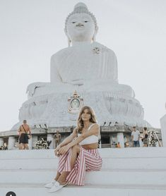 a woman sitting in front of a white buddha statue