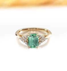 This stunning ring is a perfect blend of timeless elegance and modern sophistication, designed to capture the essence of luxury in every detail. The centerpiece is an exquisite emerald-cut mint green sapphire, known for its vibrant, rich hue that radiates a sense of calm and refinement. The main stone's clean lines and geometric shape are enhanced by its vivid color, making it a truly captivating focal point. Surrounding the mint green sapphire are clusters of sparkling diamonds, carefully arran Emerald Cut Amethyst Ring, Green Emerald Cut Diamond Ring With Rose Cut Diamonds, Fine Jewelry Green Sapphire Ring With Rose Cut Diamonds, Green Sapphire Ring With Rose Cut Diamonds, Green Timeless Diamond Wedding Ring, Green Diamond Ring With Rose Cut, Exquisite Green Diamond Ring With Center Stone, Elegant Green Sapphire Promise Ring, Elegant Green Round Cut Sapphire Ring