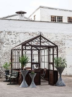 an outdoor area with potted plants and two vases on the ground next to a white brick wall