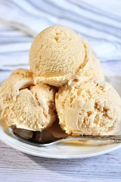 three scoops of ice cream on a white plate with a spoon next to it