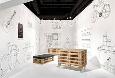 a white room with drawings on the wall and wooden pallets in front of it