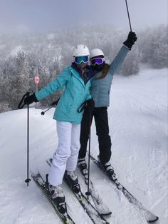 two people on skis posing for the camera with their arms up in the air