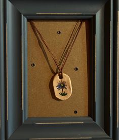 a wooden frame with a ceramic flower and palm tree on the front, hanging from a cord