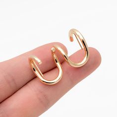 a person is holding two small gold hoops in their hand, with the top one open