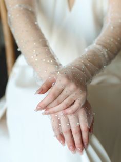 a woman in a white dress holding on to her hand with beaded mesh sleeves